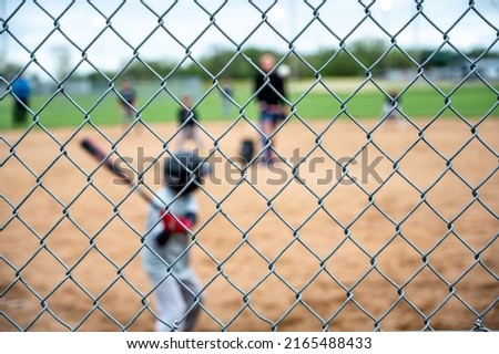 Selective focus on chain link fence with a youth baseball game defocused and blurred in the background