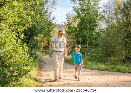 Front view of grandfather with hat and grandchild walking on a nature path Royalty-Free Stock Photo #216548914