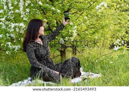 selective focus. A beautiful brunette girl in nature takes a picture on a mobile phone. A girl takes a selfie against the background of an apple tree