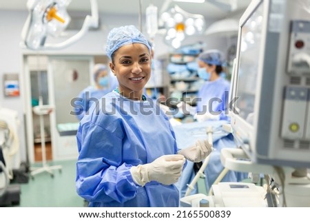 Anesthesiologist checking monitors while sedating patient before surgical procedure in hospital operating room. Young adult female African American patient is asleep on operating table during surgery.