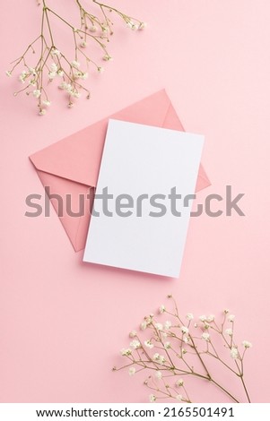 Party invitation concept. Top view vertical photo of pink envelope paper sheet and white gypsophila flowers on isolated pastel pink background with empty space
