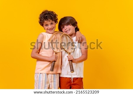 Portrait of two brothers playing tennis on summer vacation, yellow background
