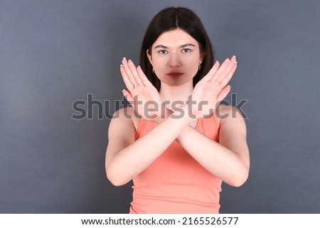 Caucasian woman wearing orange sportswear over studio grey wall has rejection expression crossing arms and palms doing negative sign, angry face.