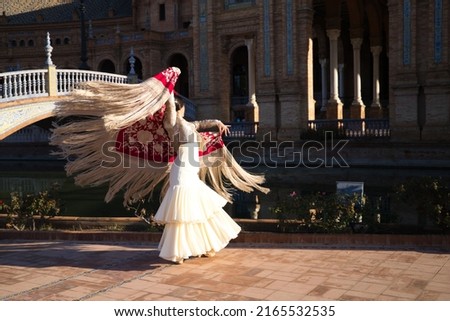 Flamenco dancer, woman, brunette and beautiful typical spanish dancer is dancing with a red manila shawl in a square in seville. Flamenco concept of cultural heritage of humanity. Royalty-Free Stock Photo #2165532535