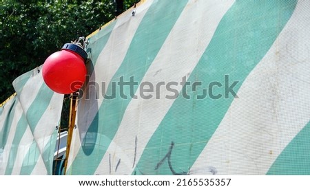 Fence enclosing the construction site for safety reasons, made of thick dense fabric with green stripes and signal red round lights.