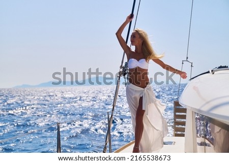 Beautiful young blond woman in bikini standing on catamaran at sunny summer day