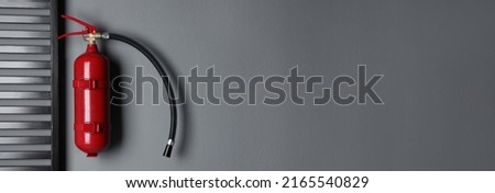 Fire extinguisher hanging on grey wall indoors, space for text. Banner design