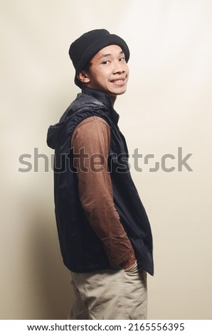 portrait of asian youth in cool pose wearing hat, brown t-shirt and black vest isolated on background