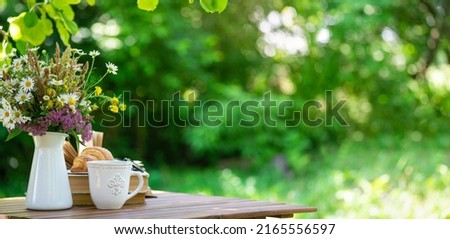 Bouquet of meadow flowers, croissant, cup of tea or coffee, books on table in summer garden. Rest in garden, reading books, breakfast, vacations in nature concept. Summertime in garden on backyard Royalty-Free Stock Photo #2165556597