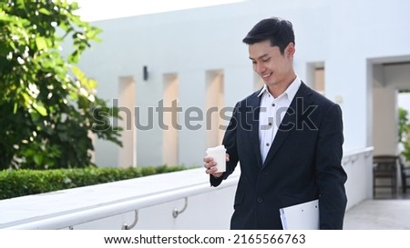 Successful young businessman holding coffee cup and walking at modern office district