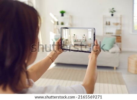 Person who plans on selling house or big spacious studio apartment takes photo on tablet device of clean bright Scandinavian Nordic home interior with stylish sofa, shelves, light walls, large windows Royalty-Free Stock Photo #2165569271