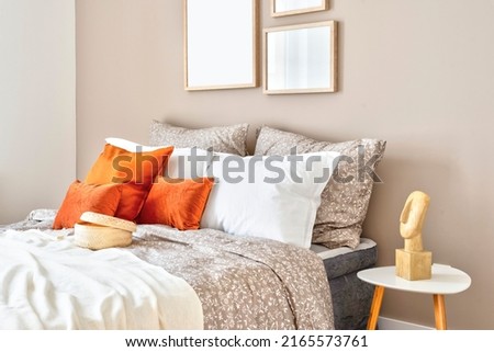 Comfortable double bed with red piloows, white bedding and blanket in cozy bedroom. Stylish interior in hotel with frame on the wall. Modern room in apartment at home.