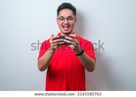 Portrait of young Asian man wearing casual shirt playing online game on mobile phone isolated over white background