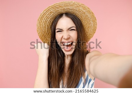 Close up young fun happy woman 20s in summer clothes striped dress straw hat doing selfie shot on mobile phone do winner gesture clench fist isolated on pastel pink color background studio portrait.