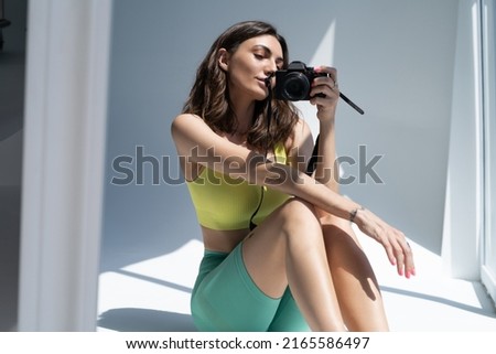A beautiful young athletic woman in leggings and a top takes a selfie photo on the camera, takes a picture of herself in the mirror and smiles