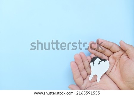 Tooth decay and dental cavities care concept. Top view of hands holding a big white tooth with black dental caries cutout in blue background with copy space. Royalty-Free Stock Photo #2165591555