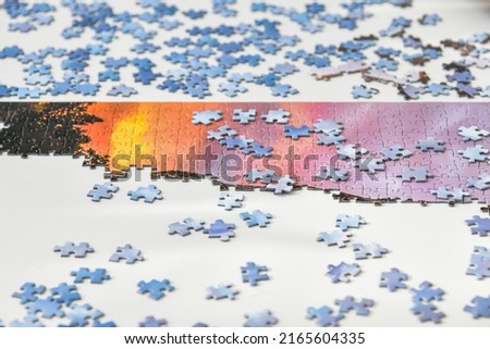 Scattered puzzles lie on the table and part of the assembled picture.