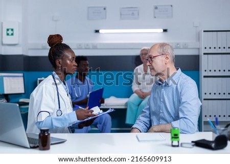 Healthcare clinic specialist taking notes about sick elderly patient health condition while recommending advanced consultation and examination. Hospital practitioner writing on clipboard illness Royalty-Free Stock Photo #2165609913