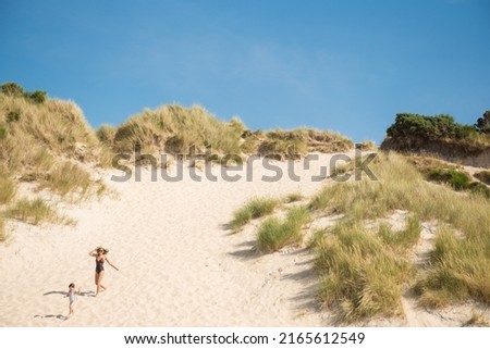 A young woman wearing a swimming suit and a hat and her daughter's run down  a white sand beach under a blue  in Camusdarach Beach, Mallaig, Scottish Highlands, UK