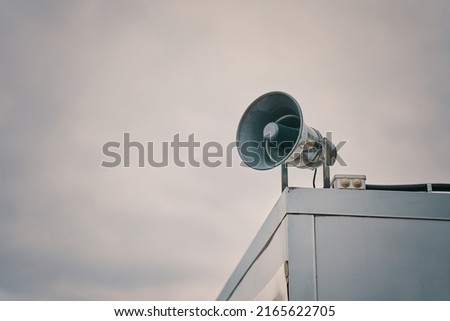 Megaphone on cloudy sky background. Providing security in town, notification of emergencies. Emergency alert siren. City hazard warning system. Copy space for text. Royalty-Free Stock Photo #2165622705