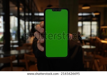 man showing green screen mobile phone at cafe vertically
