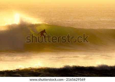 A surfer catches some early morning waves as the sun glows on the day