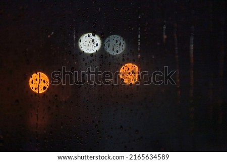 Abstract background with raindrops on window and night blurred light. Rain drops on glass for backgrounds rainy fall autumn weather. Outside window is blurred bokeh water of night city