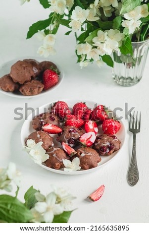 A white plate with fresh chocolate cakes with cranberry and strawberry . Morning table with fresh gluten free muffins and jasmine flower.
