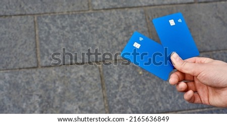 The hand holds two blue bank cards against the background of granite paving stones. Space for text.