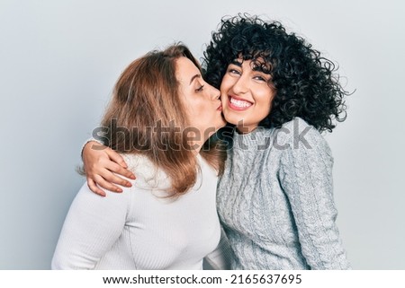 Young brunette woman and senior woman standing over isolated background. Daughter and mother hugging and bonding together as happy family