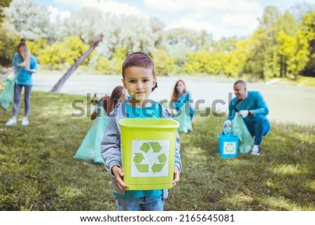 A multiethnic group of school children of different ages who recycle and collect garbage in their local park. A young team of volunteers is happy to clean up their community.