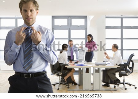 Businessman with fingers crossed and co-workers working in background