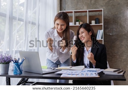 Excited two young Asian woman in the office, triumph reading good unexpected news or email on laptop. Overjoyed Asian female look at computer screen feel euphoric win lottery online.