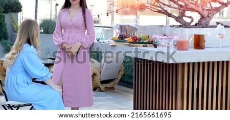 Banner with a girl in a pink dress at an event is talking to her friend. Background - the roof of the penthouse, fruits and drinks. Buffet, Party, meeting, holiday.