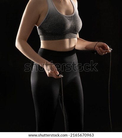 Close up picture of athletic woman performing exercise with jumping rope on the black background