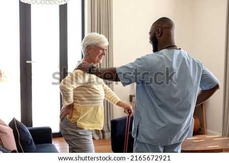 African american male health worker helping caucasian senior woman to walk using a walking stick. Medical care and retirement senior lifestyle concept