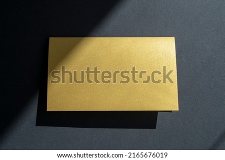 Golden business card mockup, invitation on black surface with shadows and sunlight