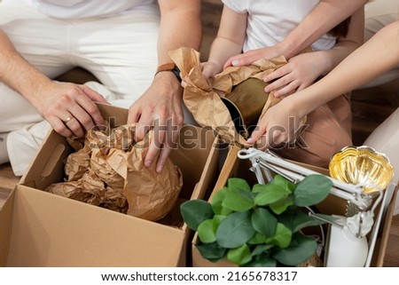 Close-up photo of a young family packing their belongings before moving to a new apartment building wrapping them in protective paper and hiding them in cardboard boxes.