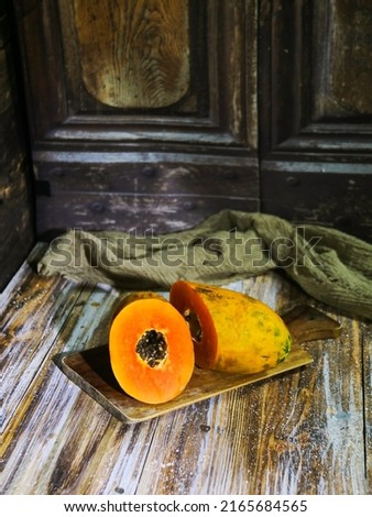 Papaya fruit (tropical friut) in halves is placed on a cutting board, the seeds are visible, on a wooden background, darkmood, indoor studio
