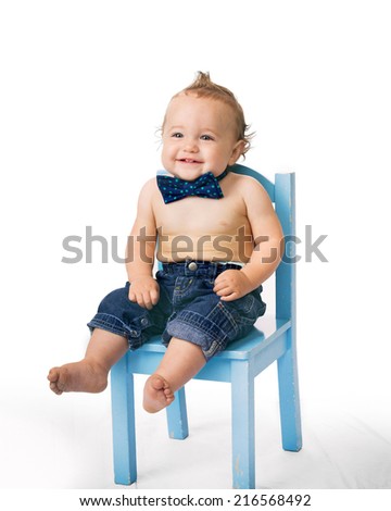 One year old boy wearing bow-tie sits in small blue chair for his birthday portrait.