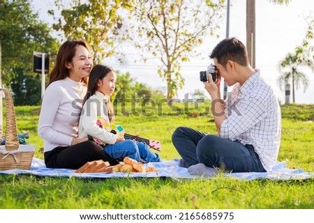 A little girl takes a picture of her parents (Father, Mother) during picnic. Family weekend