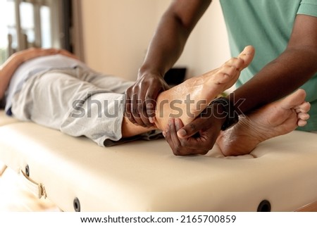 African american male physiotherapist giving foot massage therapy to caucasian senior woman at home. Physiotherapy and rehabilitation concept Royalty-Free Stock Photo #2165700859