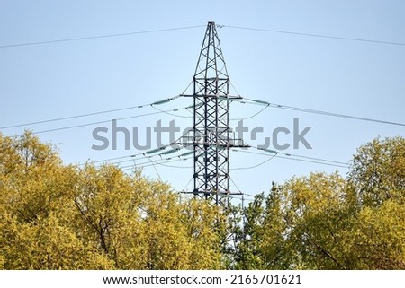 High metal pillar with high-voltage electric wires against background of blue sky. Green trees in spring.