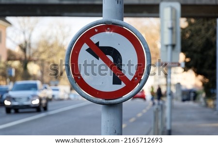 old damaged traffic sign, no left turn, black arrow on white background, red strikethrough, car with daylight blurred in background, in daytime