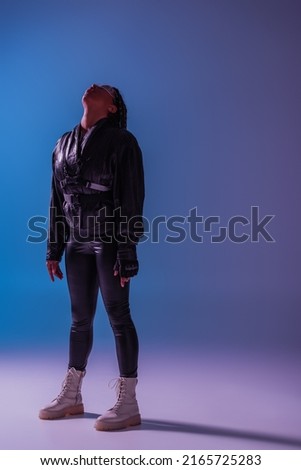 Full length of stylish african american woman in smart glasses standing on blue and purple background