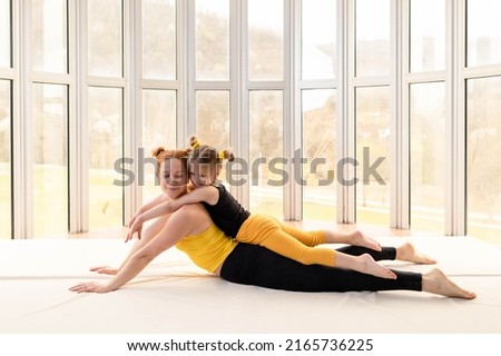 Little girl lying on top of her fit mother in the gym