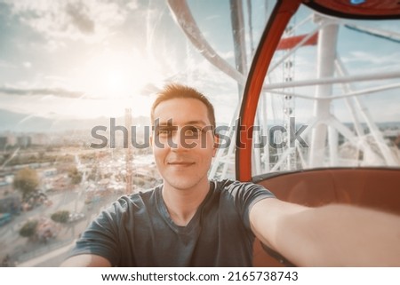 Happy and excited young man taking selfie photo in cabin of a ferris wheel. Solo travel adventures and amusement park