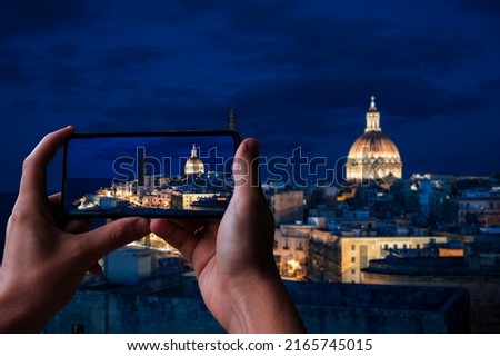 Tourist taking photo of illuminated at night Valletta old town and harbor in Valletta, Malta.