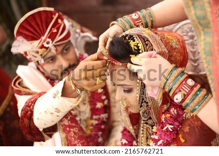 Indian bride and groom wearing traditional dress, Indian Bride and groom posing on their wedding, Indian groom dressed in white Sherwani and red hat with stunning bride in dark red lehenga Royalty-Free Stock Photo #2165762721