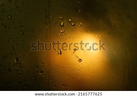 Dark background with defocused light steam warm gradient. Orange light with drops on the window glass